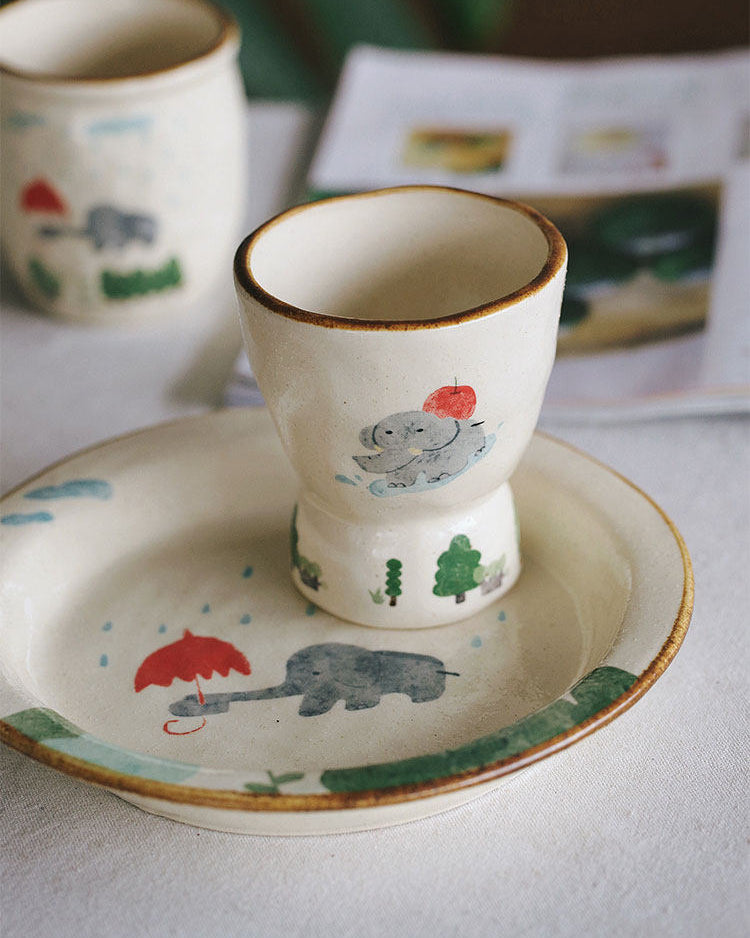 Ceramic cup and saucer with animal illustrations on a light surface.