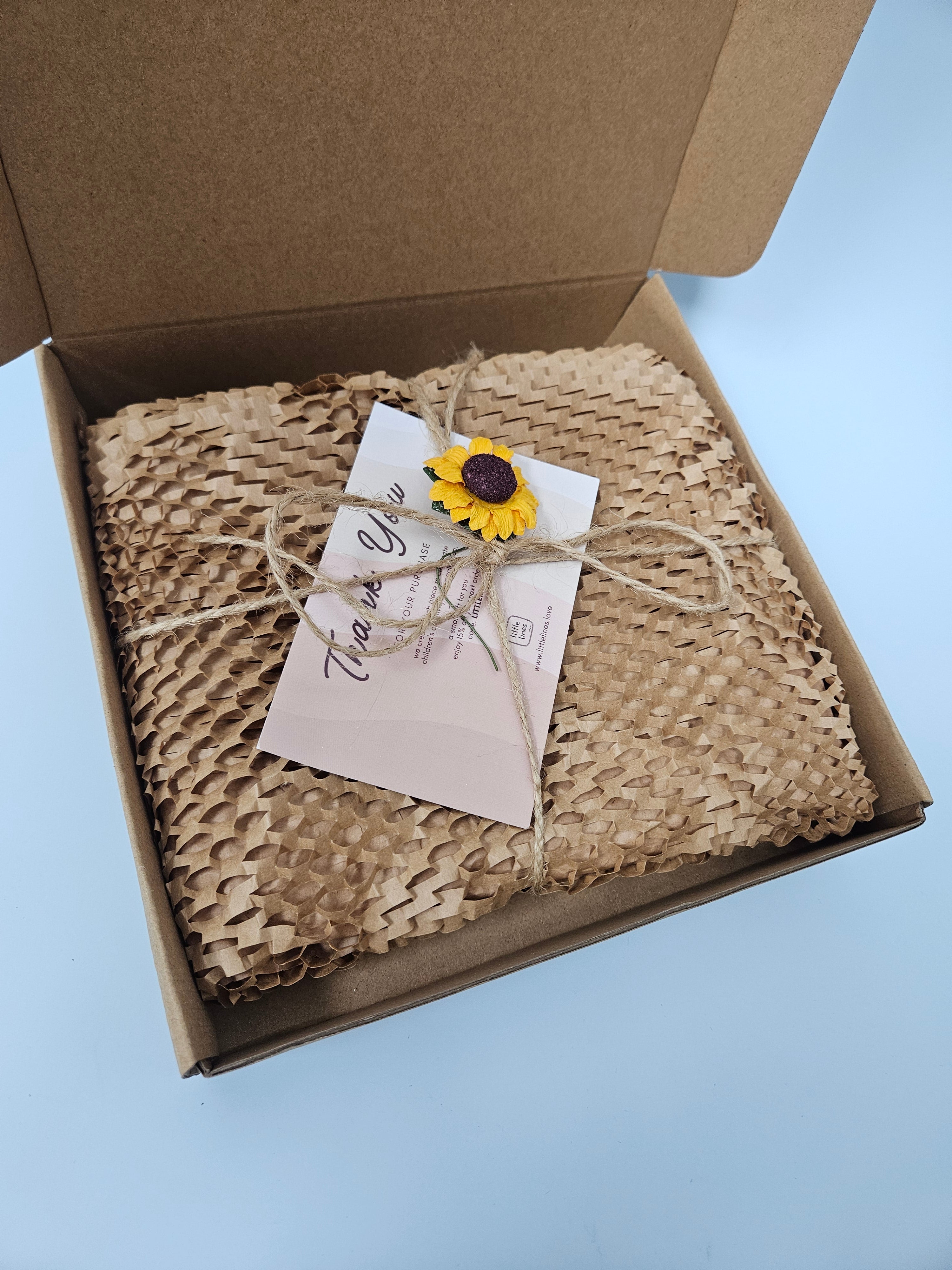 Woven blanket with a sunflower decoration and card in a cardboard box on a light blue background