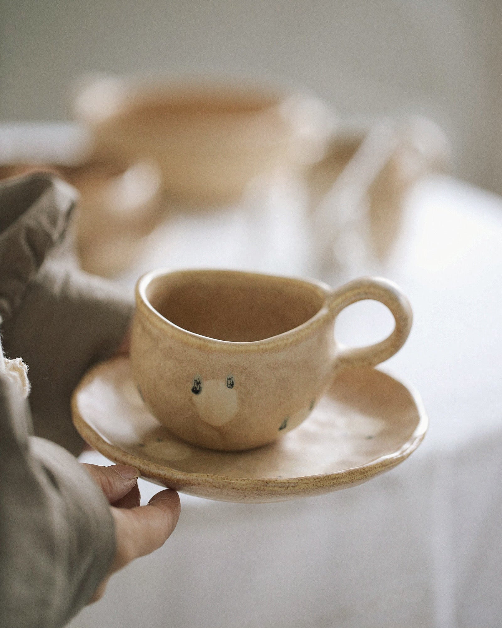 Ceramic cup with a face design on a saucer held by a person.